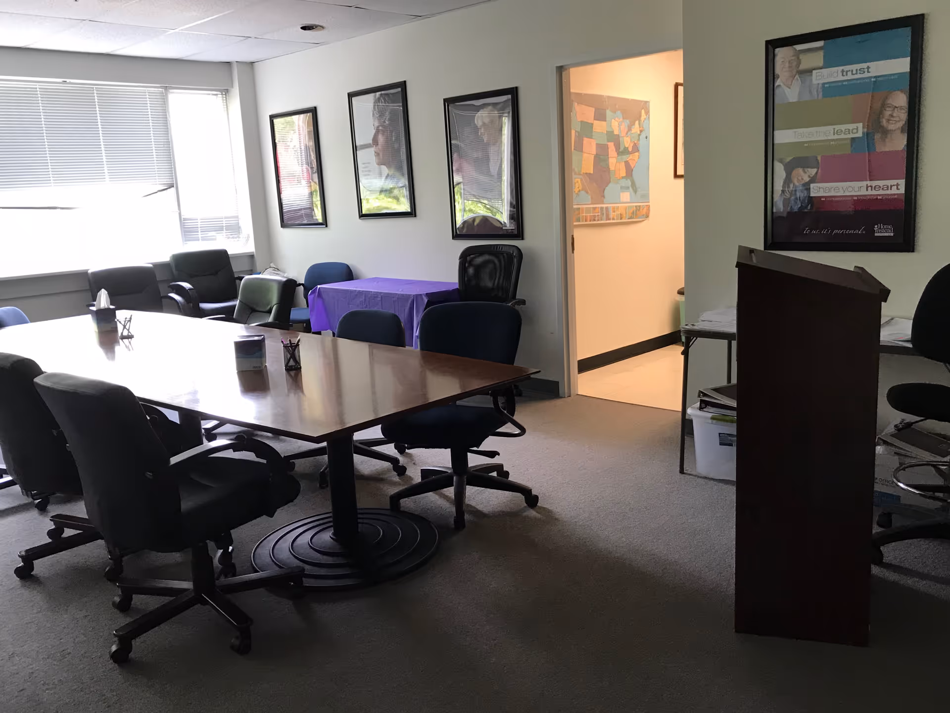A conference room with a large table, chairs, a podium, and framed posters on the walls.