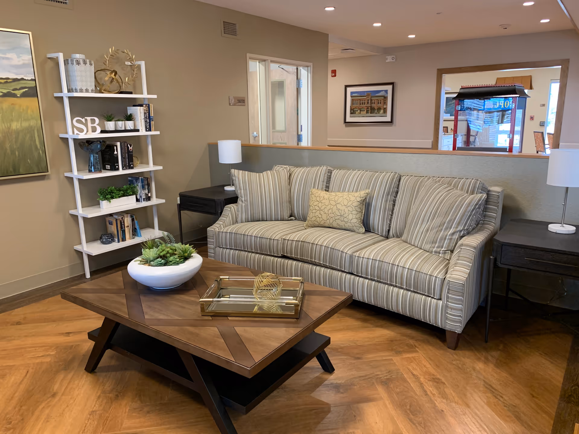 Comfortable lounge area with a striped sofa, wooden coffee table with decor, bookshelf and side tables in a common room.