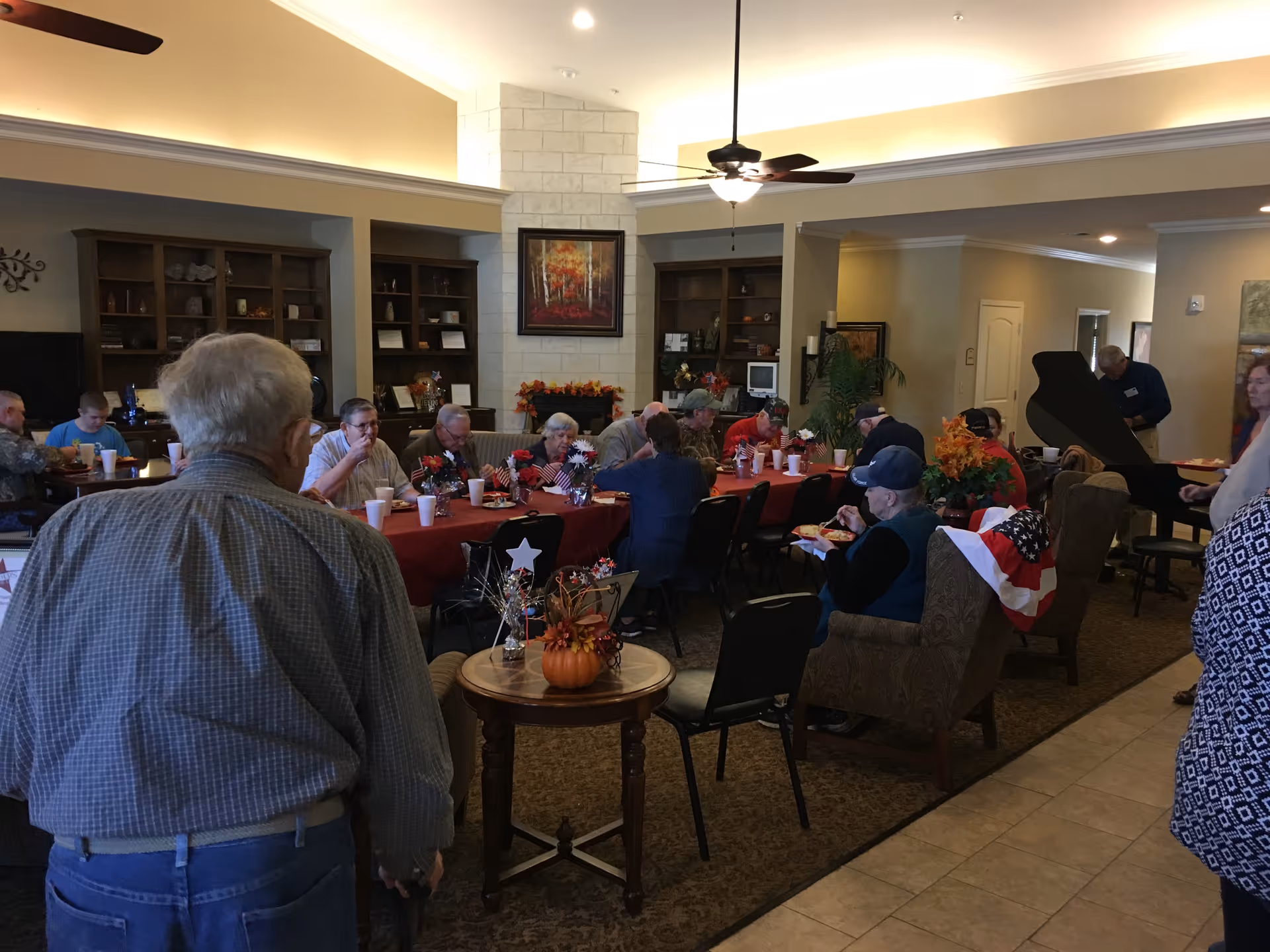 Residents gathered around a long decorated table in a communal dining area of an assisted living facility.