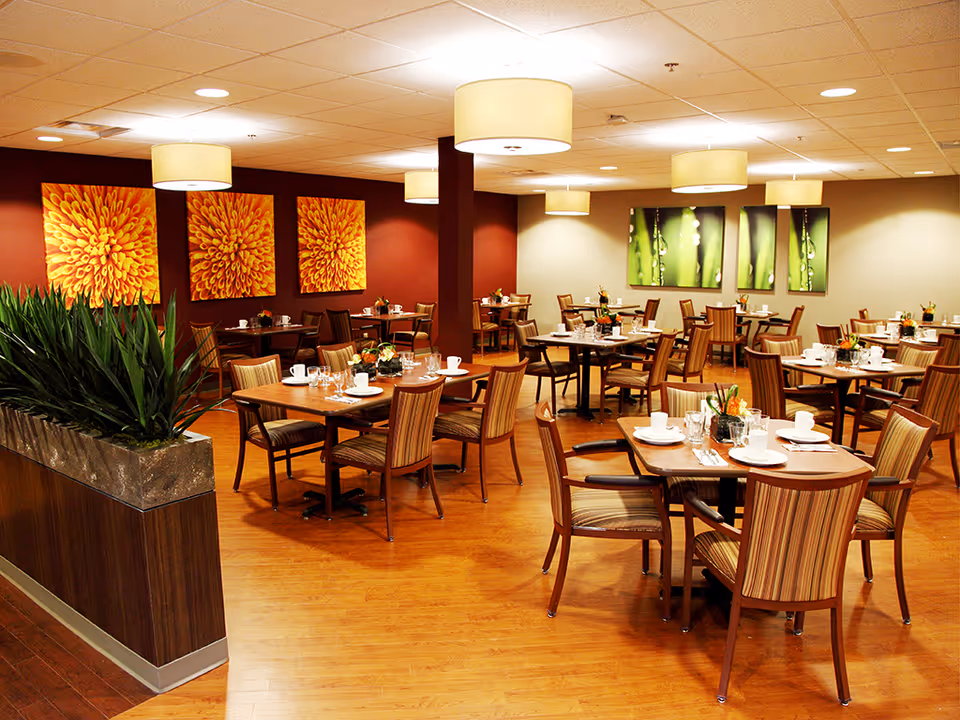 Spacious dining room in a senior living facility with arranged tables and centerpieces.