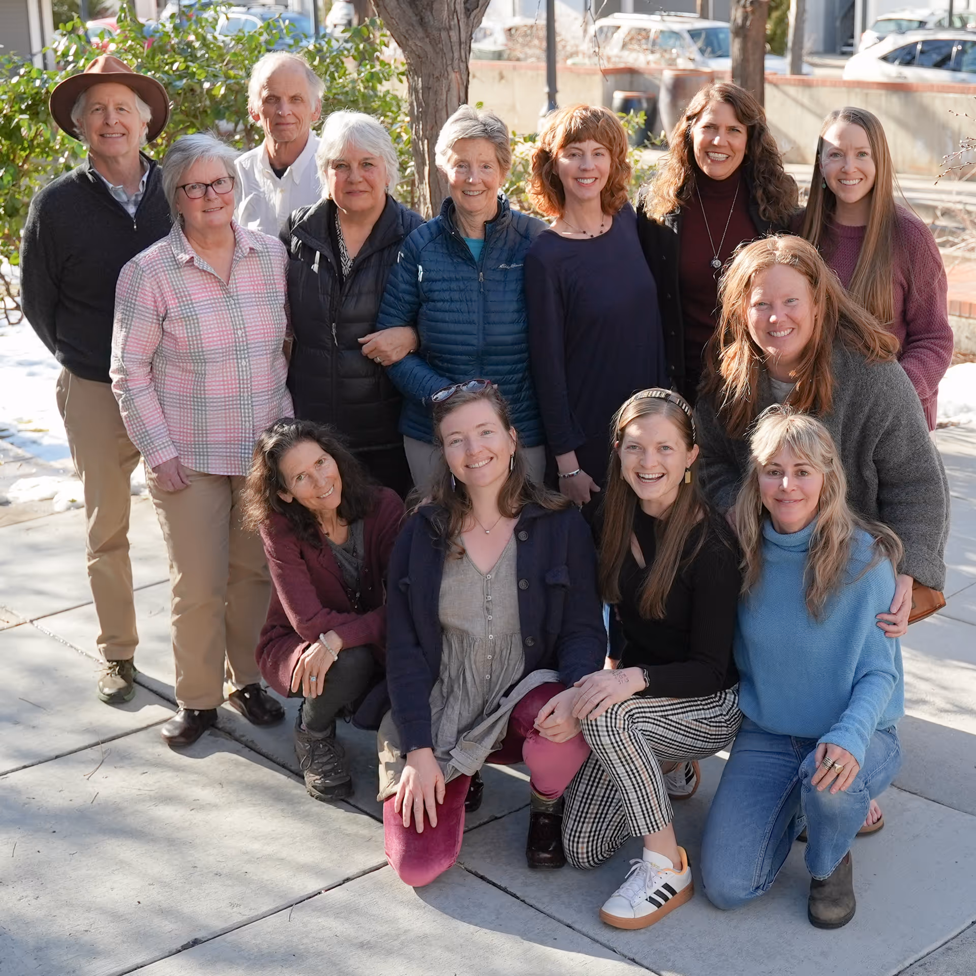 Group of adults and caregivers posing together outdoors near a tree.