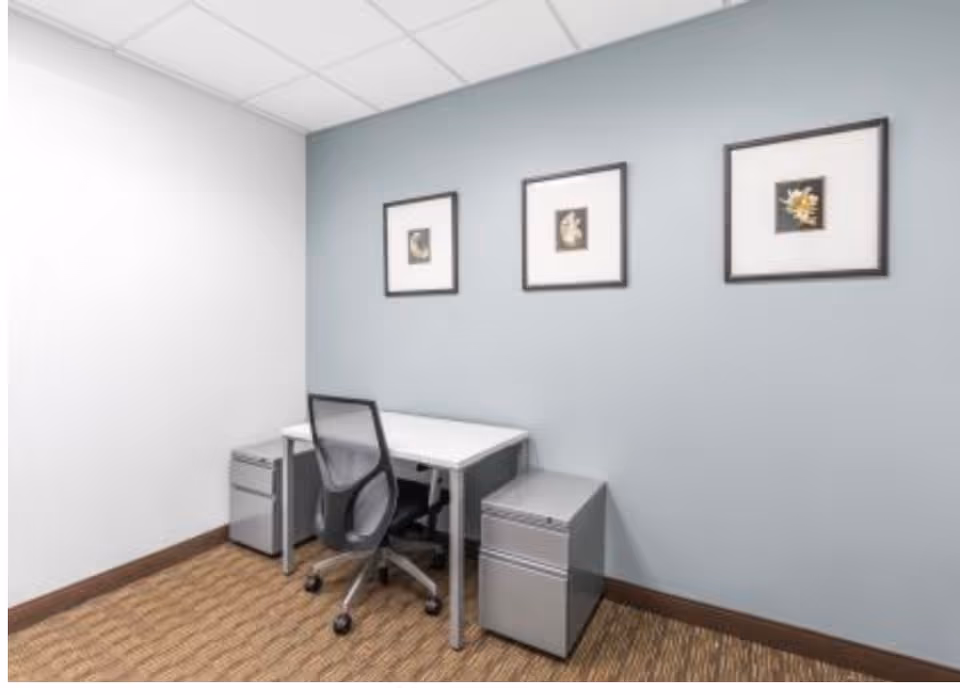 Small desk area with chair, filing cabinets, and framed art on a blue wall.