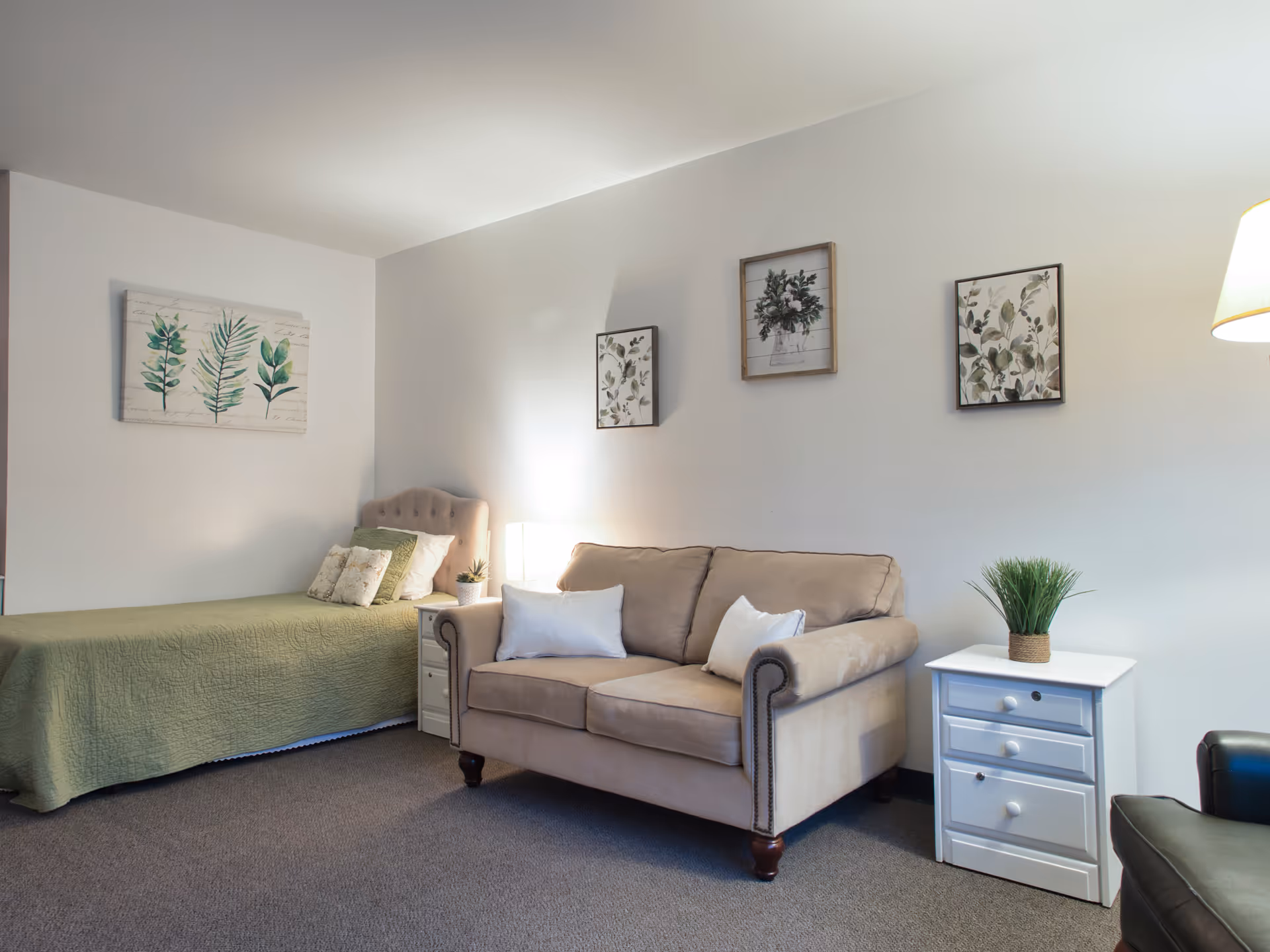 Cozy bedroom with bed, beige sofa, nightstands, wall art, and neutral decor.