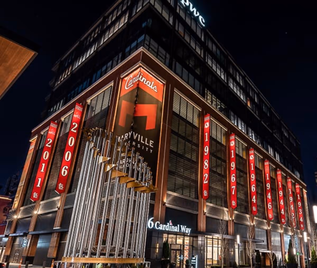 Night exterior of a tall brick building with red banners and signage along the facade.