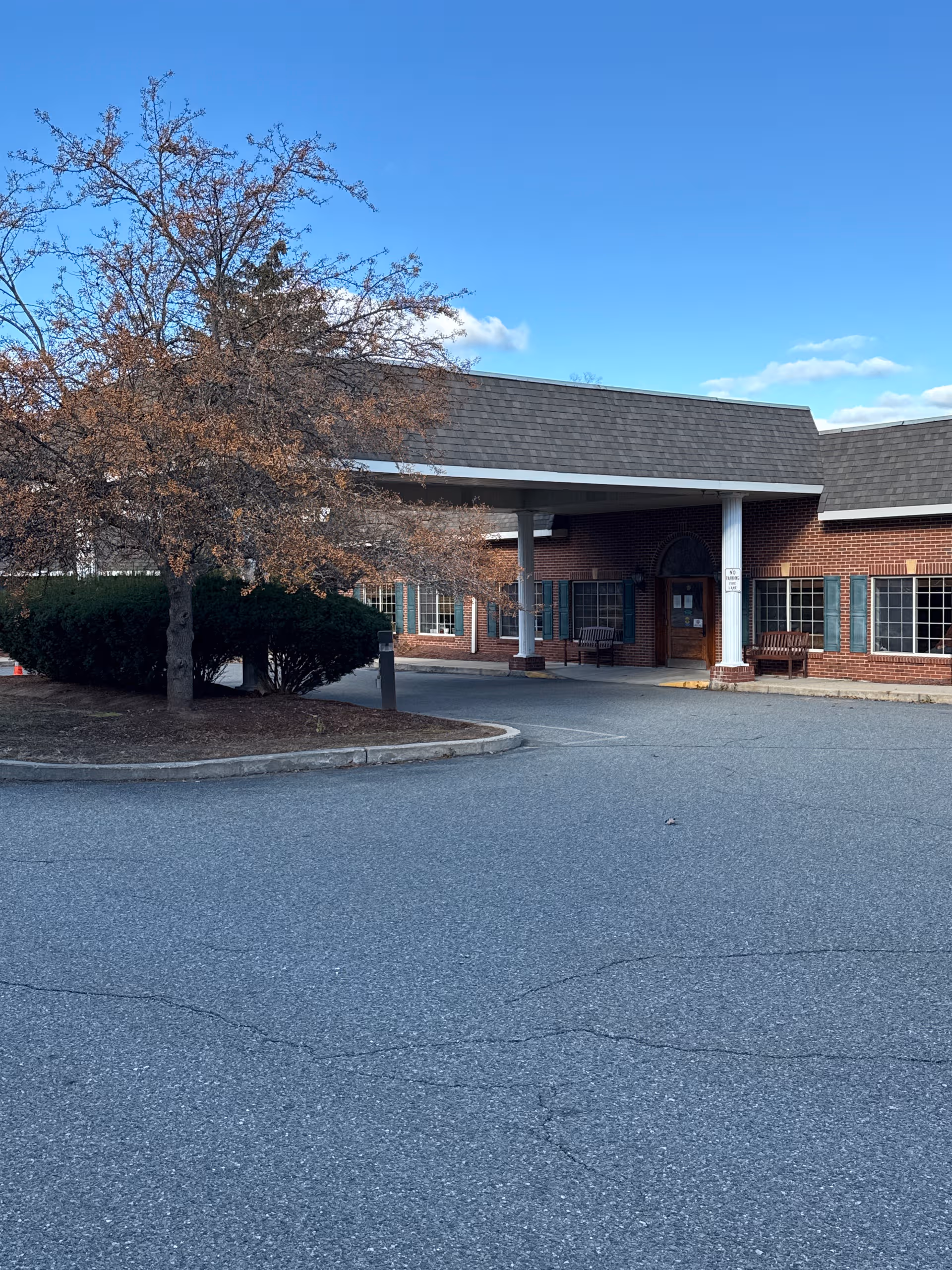 Brick senior living facility exterior with covered entrance and parking area.