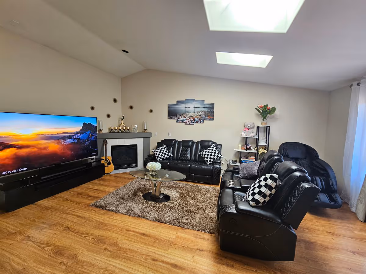 Bright living room with black leather sofas, large TV, fireplace, and decorative shelving.