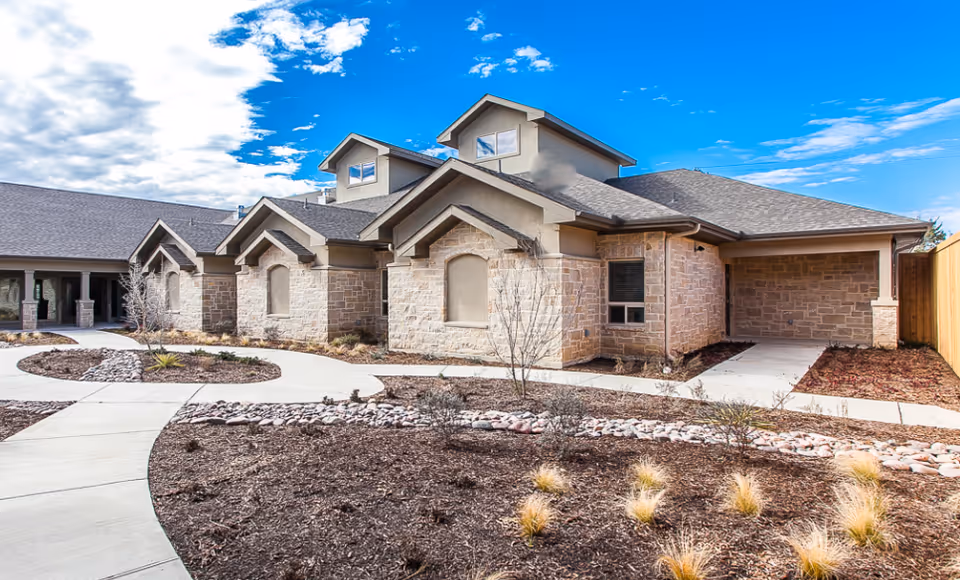 Stone-clad senior living facility exterior with curved walkway and landscaped front yard.