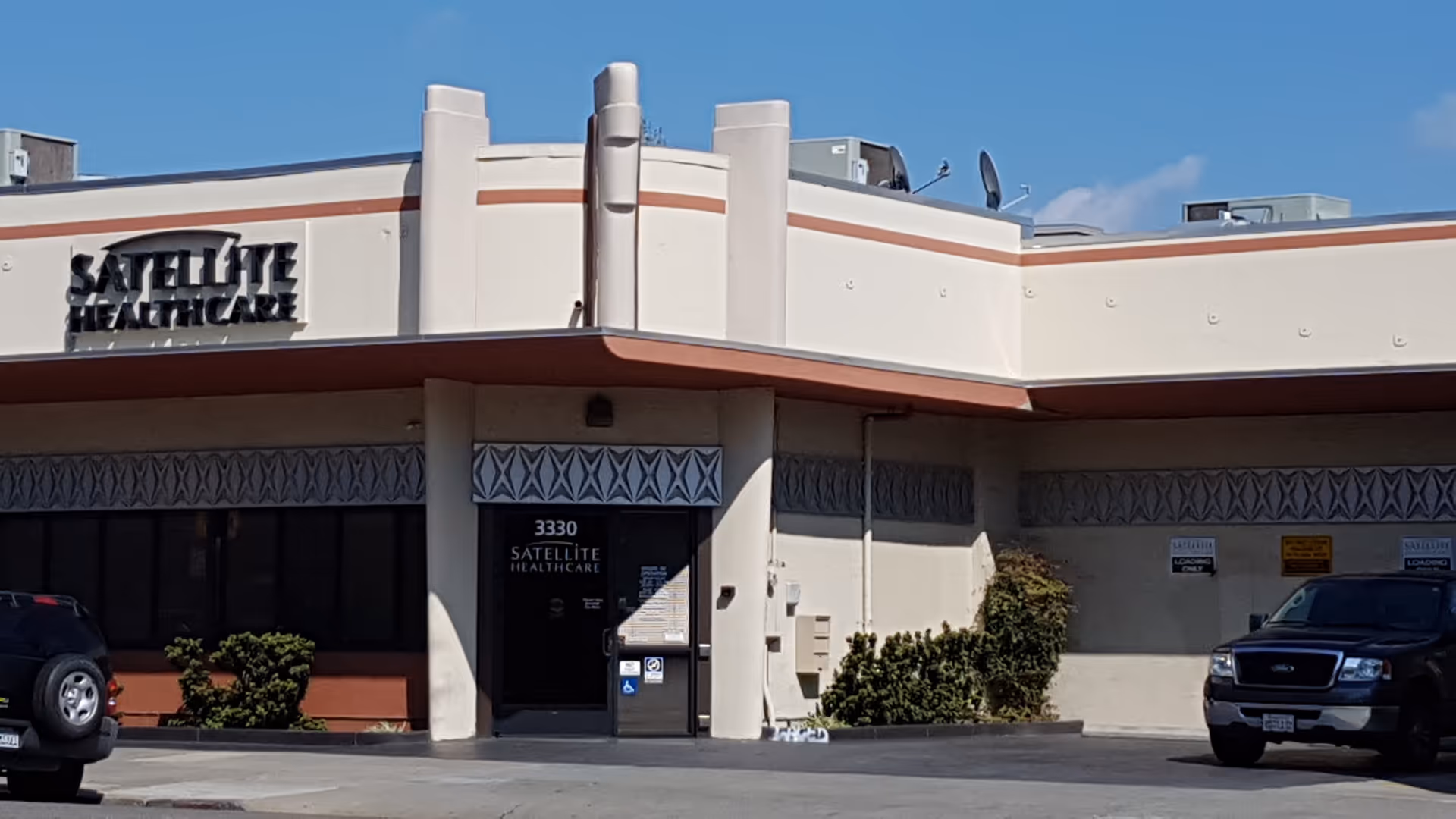 Front exterior of Satellite Healthcare facility with entrance, sign, and parked cars.