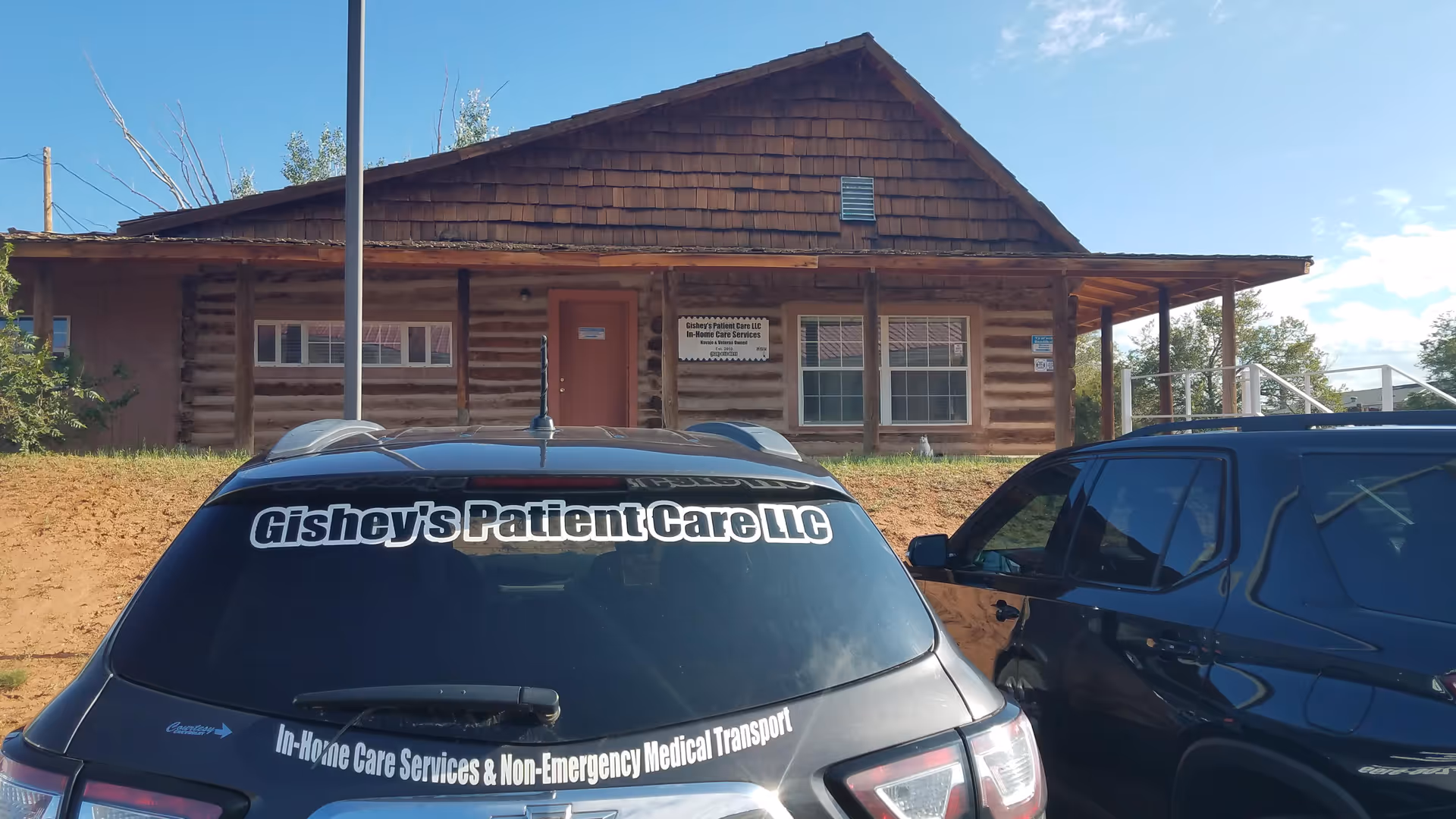 Log cabin-style building labeled Gishey's Patient Care LLC with parked cars in front.