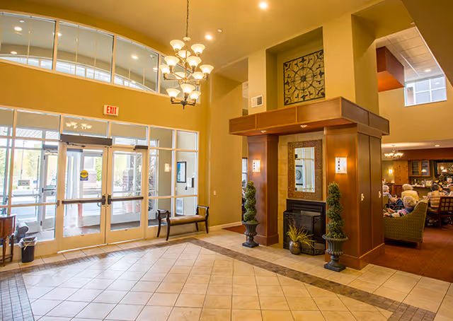 Lobby of a senior living facility with glass entry doors, chandelier, fireplace, and seating area.