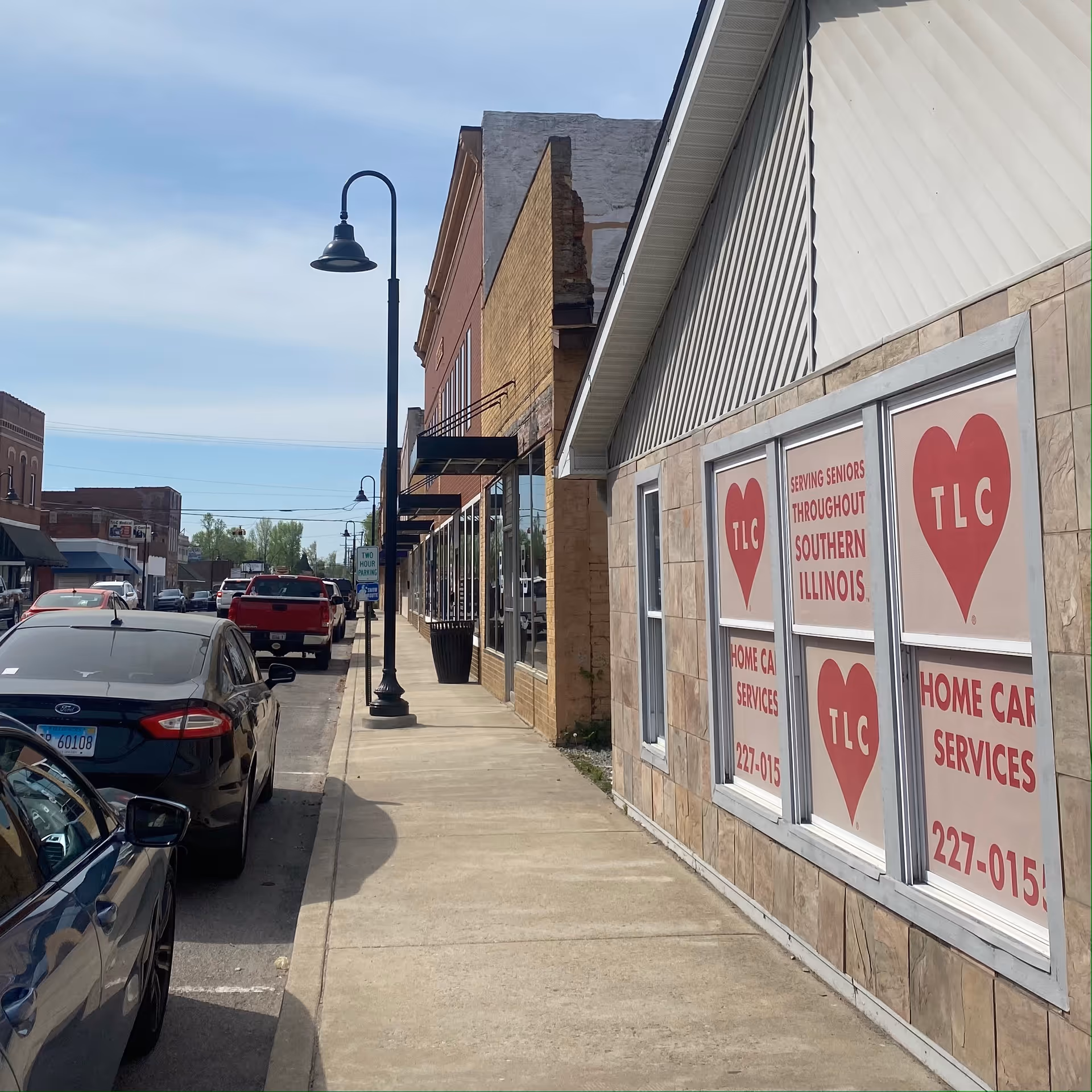 Street view of a TLC Home Care Services storefront with parked cars along the sidewalk.