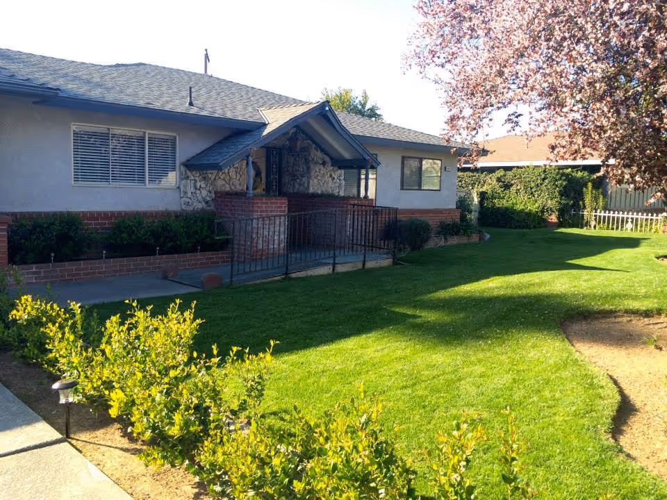 Single-story senior living facility exterior with a ramp, brick and stone entry, and well-kept lawn.