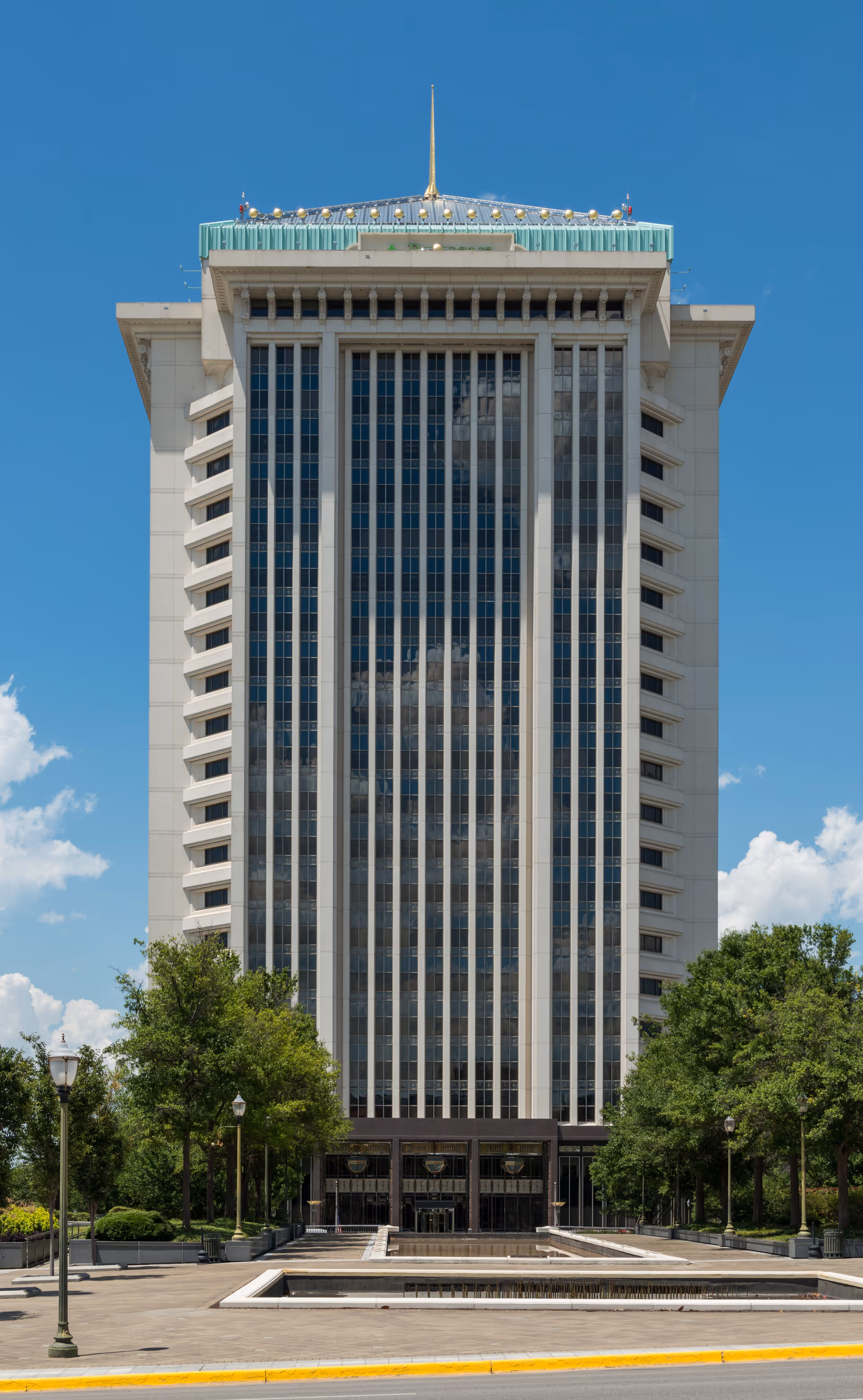Tall modern high-rise building with a grand entrance and surrounding trees.