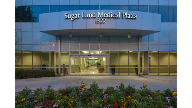 Front view of Sugar Land Medical Plaza entrance with glass doors and blooming flowers.
