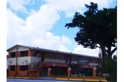 Two-story Pavilion Gardens facility exterior with brick base, white walls, and a large tree.