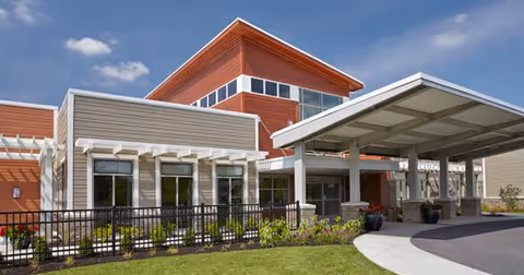 Exterior view of The Springs at Lafayette senior living facility showing a modern building with a covered entrance, large windows, and a landscaped lawn under a blue sky with some clouds.