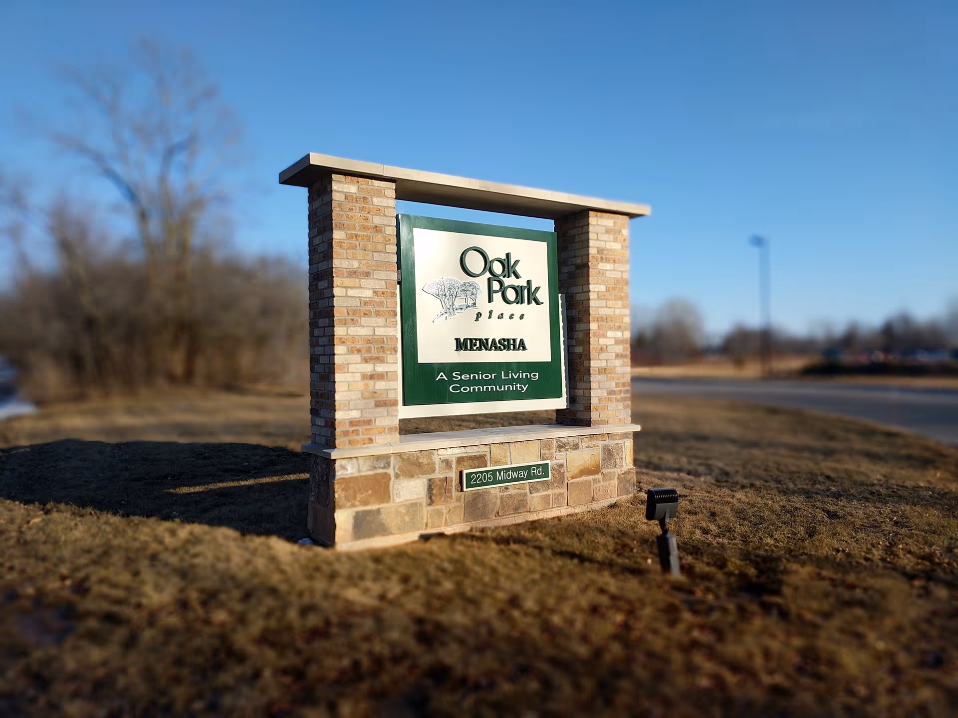 Brick sign reading Oak Park Place Menasha stands on a grassy front lawn.