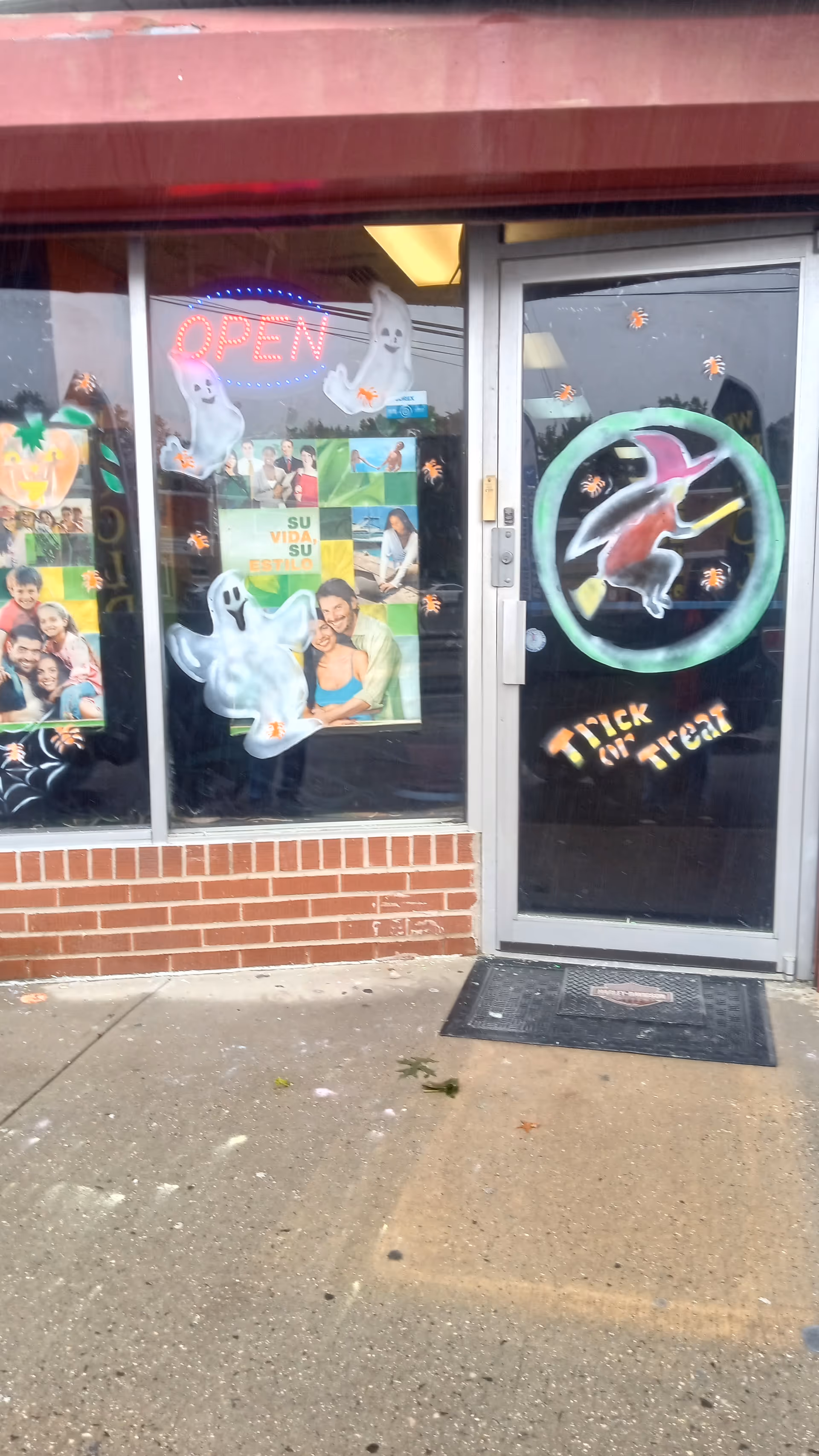 Storefront entrance decorated with Halloween ghosts, pumpkins, and an illuminated OPEN sign.