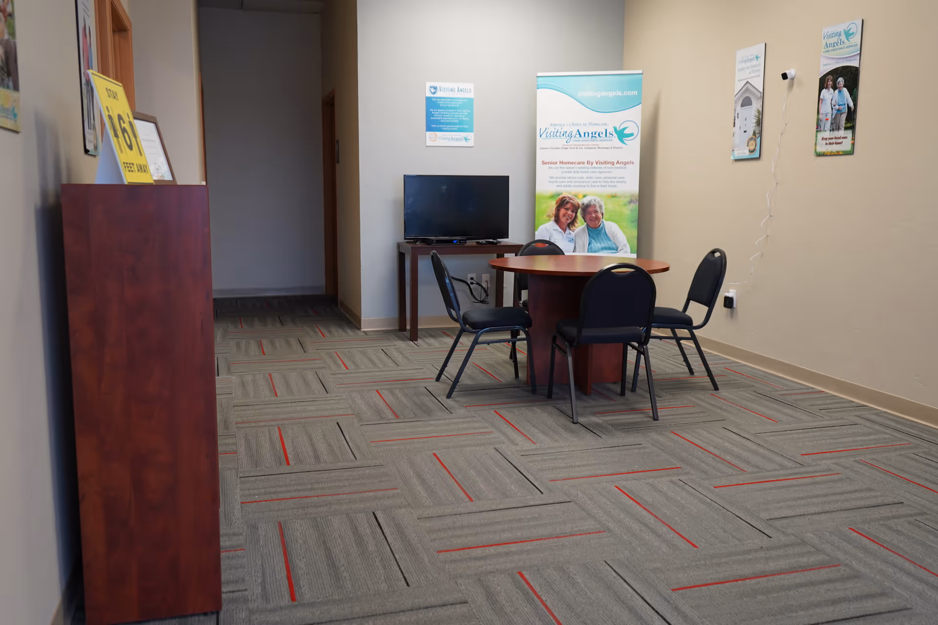 Indoor lobby area with a round table, chairs, TV, and promotional banners.