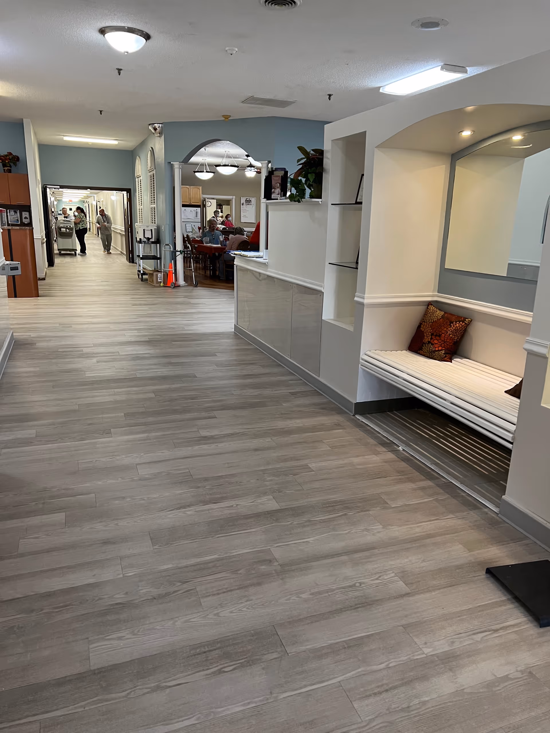 Wide interior hallway in a senior living facility with reception desk and seating alcove.