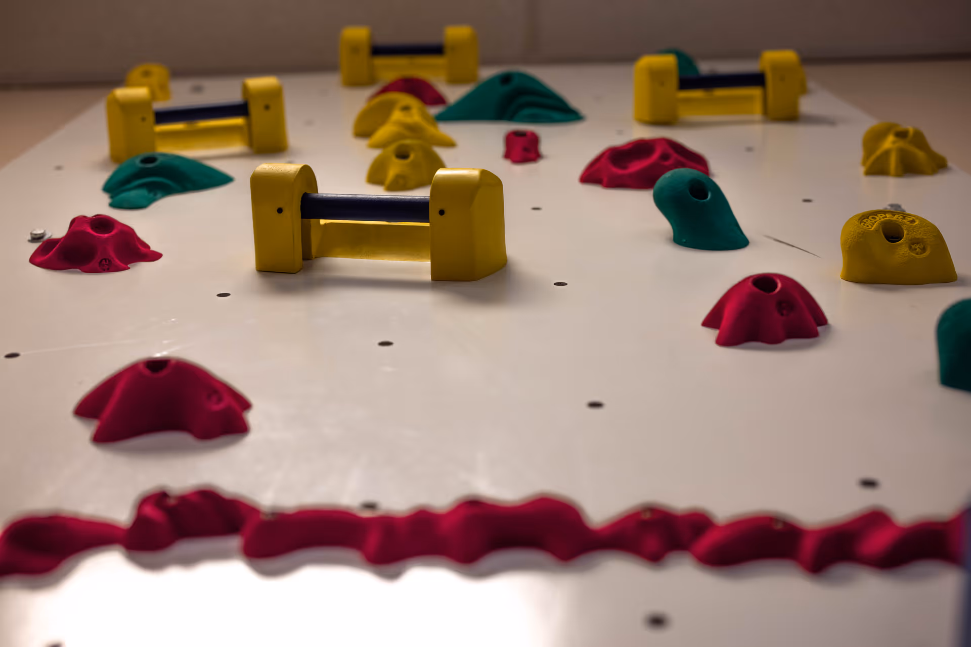 Close-up of an indoor climbing wall with multicolored holds on a white surface.