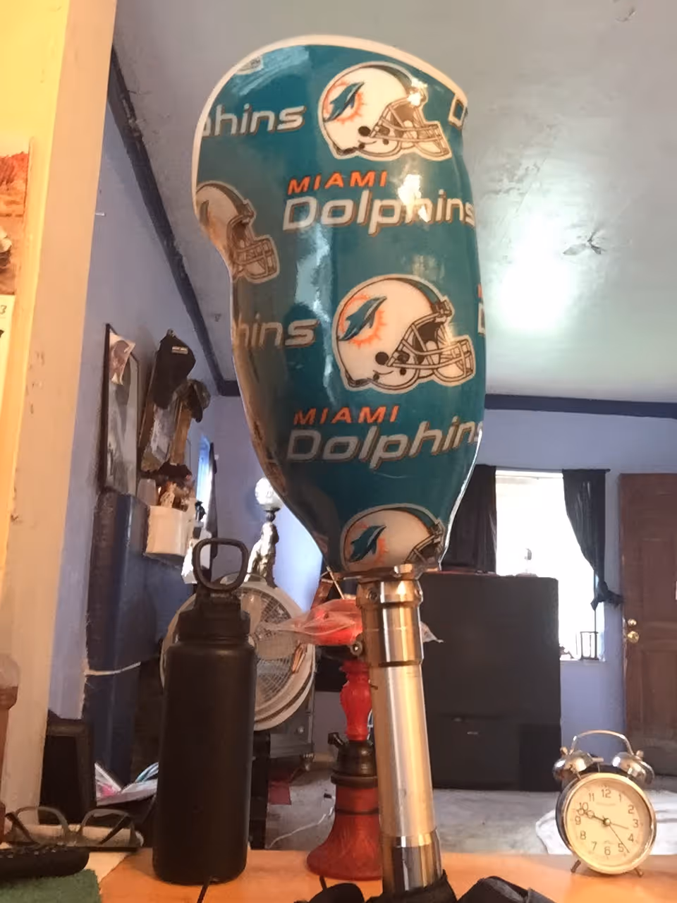 Teal Miami Dolphins punching bag indoors with a fan, clock, and assorted equipment.