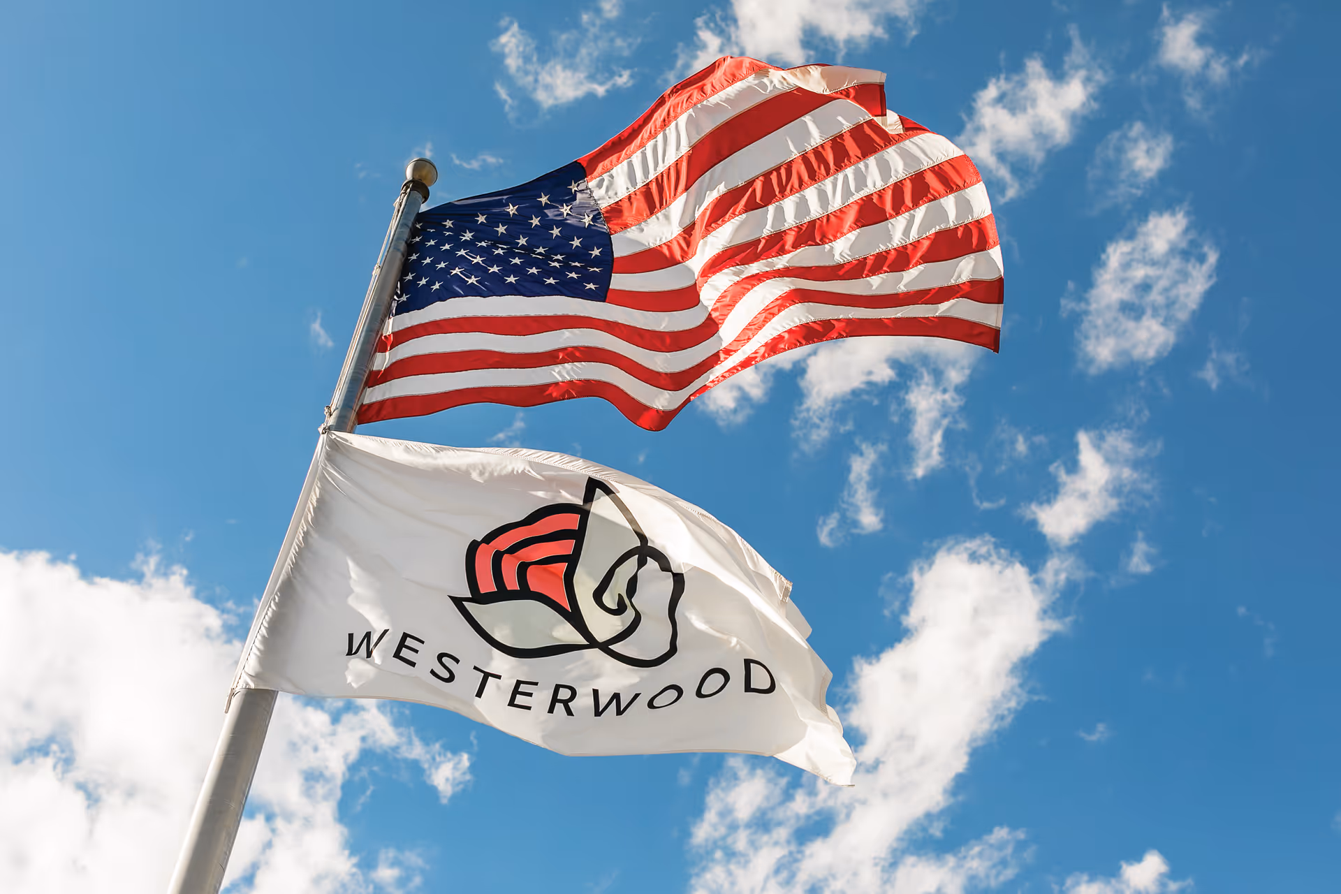 American flag and Westerwood flag flutter on a pole against a blue sky.