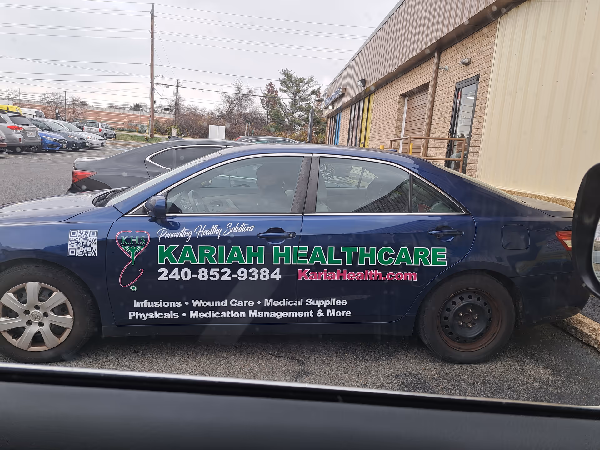 Blue Kariah HealthCare car with logo and contact info parked outside a beige building.