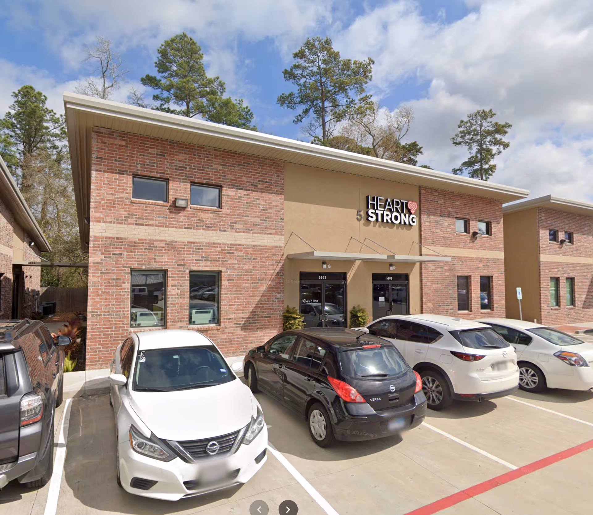 Exterior view of a brick Heart Strong senior living center with parked cars in front.