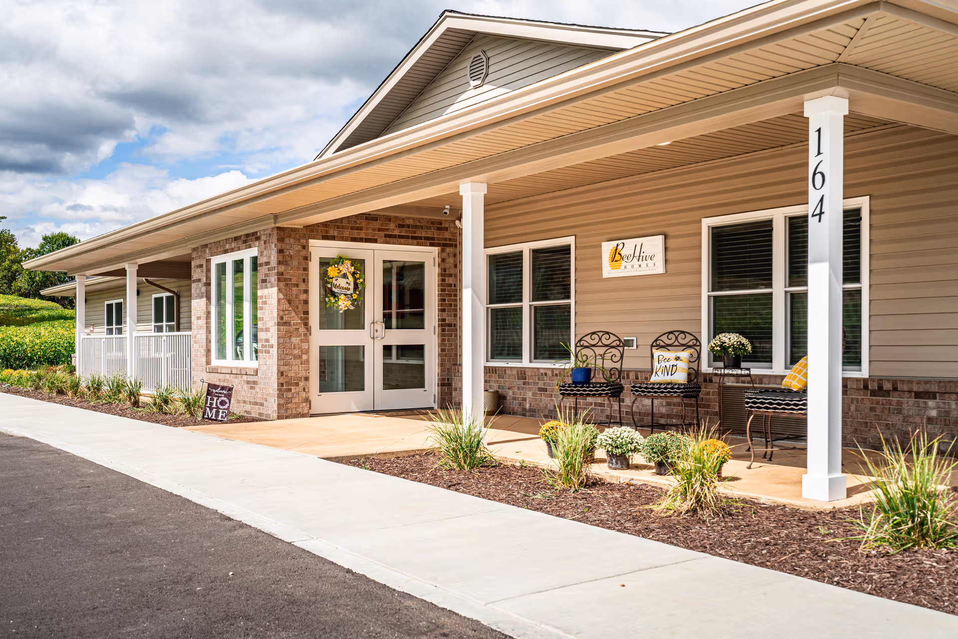 Exterior view of BeeHive Homes entrance with porch seating and brick accents.