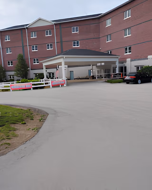Front entrance of a multi-story red-brick senior living building with a covered porte-cochere and driveway.