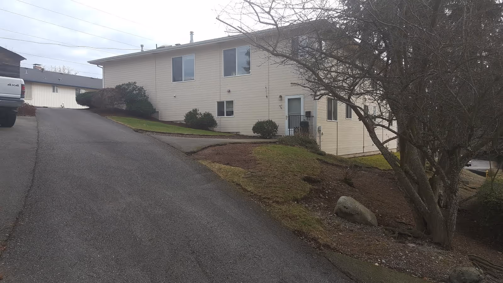 Senior living facility exterior showing a sloped driveway, beige siding, and leafless trees.