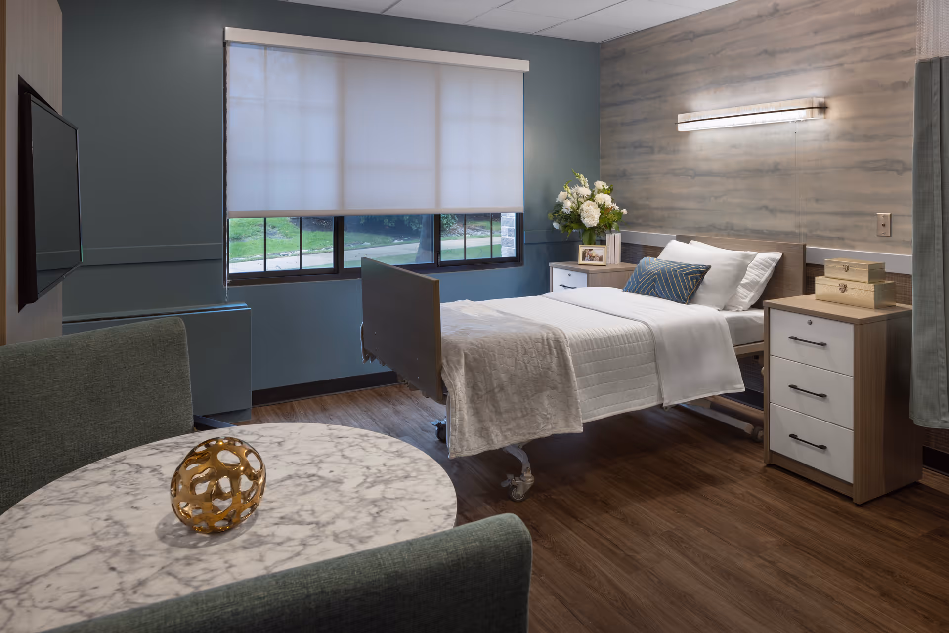 A hospital-style bed in a furnished patient room with a window and nightstands.