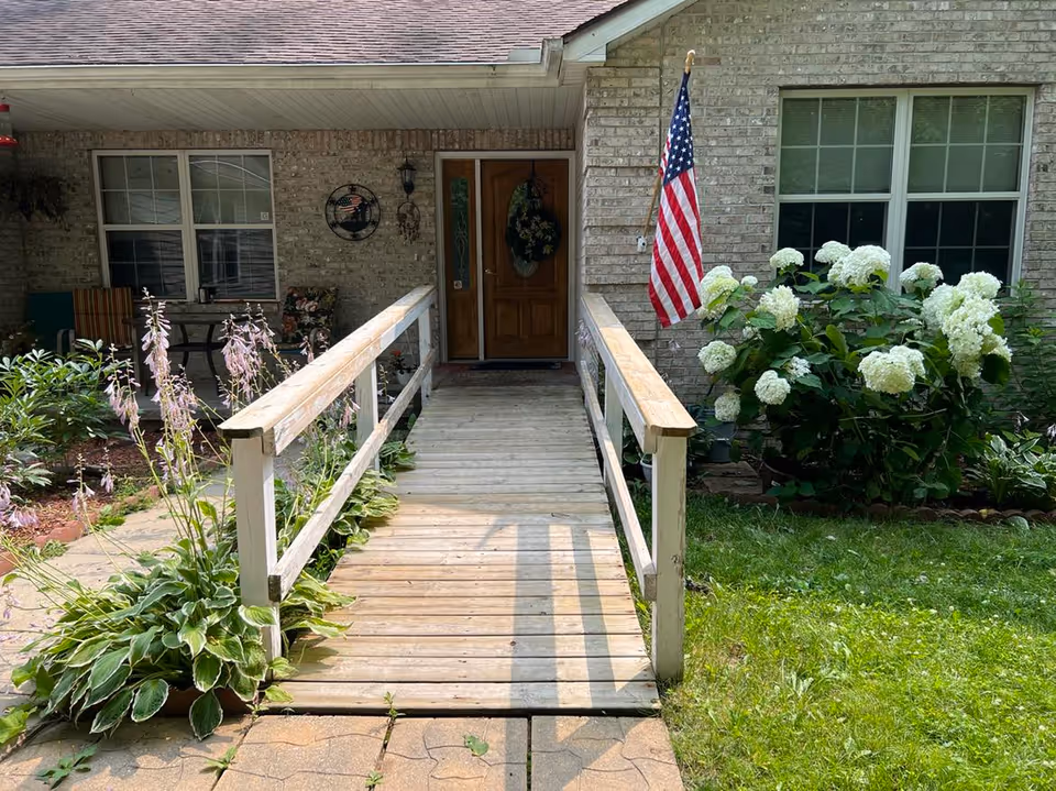 Front entrance of Loya's Assisted Living with a ramp, American flag, and hydrangea bushes.