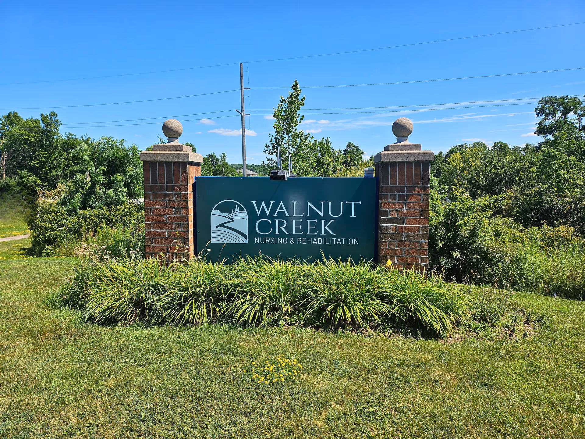 A green sign reading "Walnut Creek Nursing & Rehabilitation" mounted between two brick pillars with landscaping and trees behind.