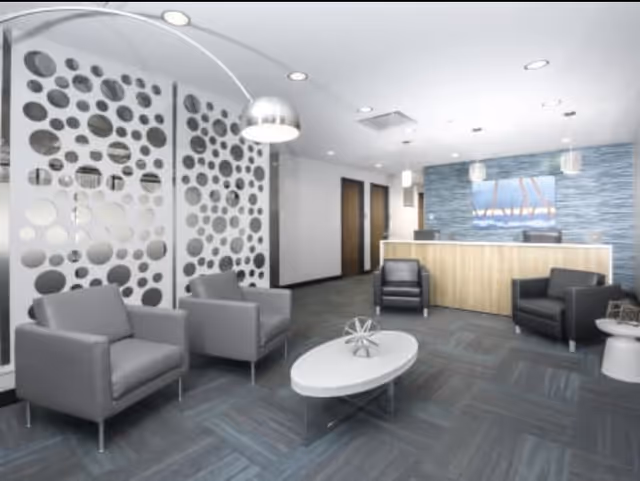 Modern interior lobby with gray lounge chairs, a circular coffee table, and a reception desk.