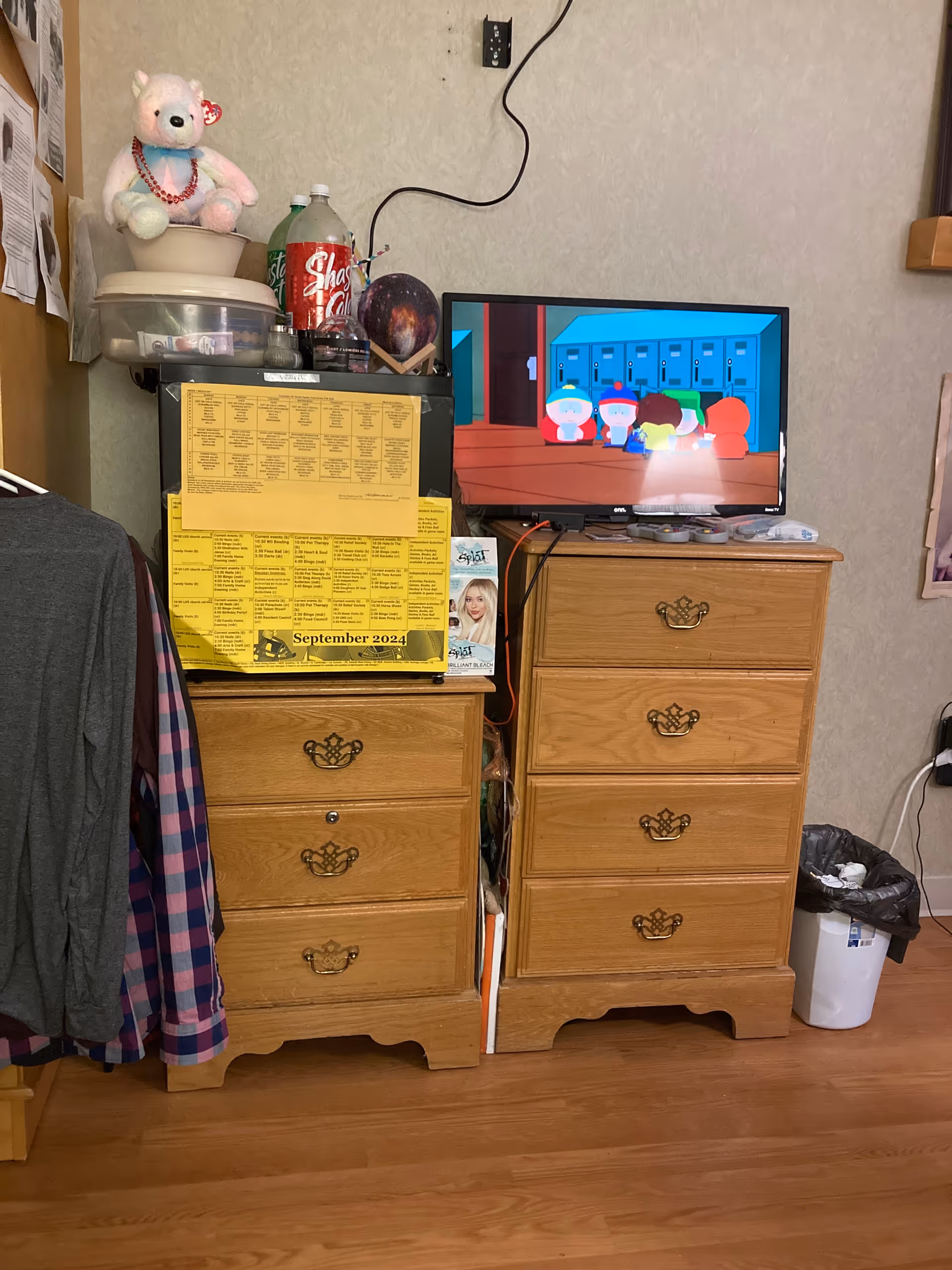 Two wooden dressers with a TV, assorted items, and a teddy bear in a cluttered bedroom.