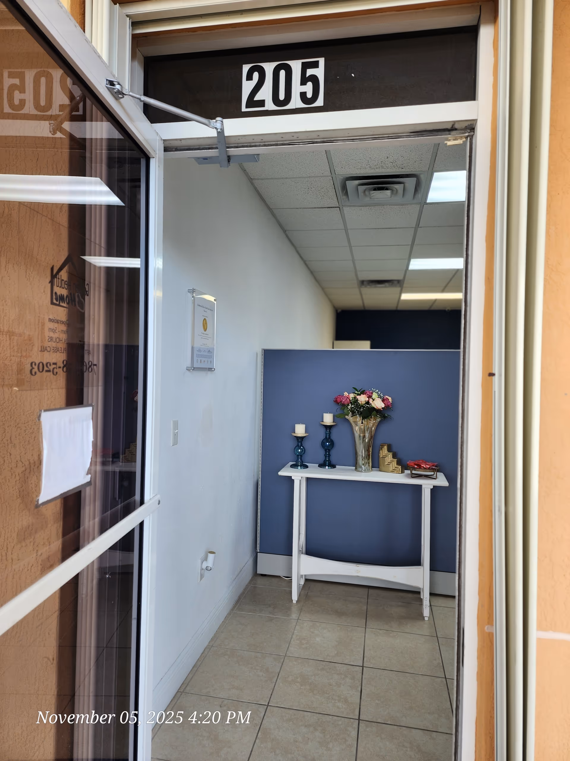 Narrow interior entry with a white table, blue partition, flowers, candles, and doorway 205