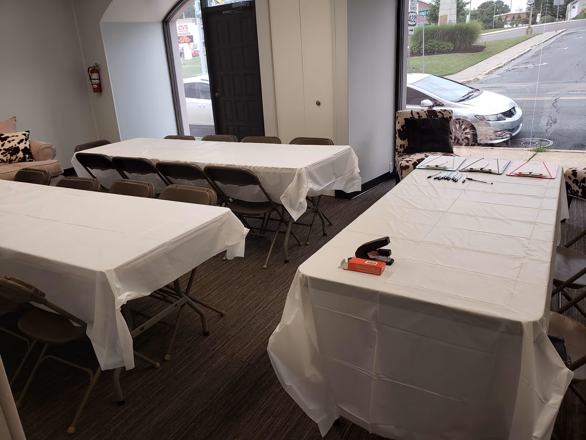 Interior conference room with long tables covered in white cloths and chairs near a window.