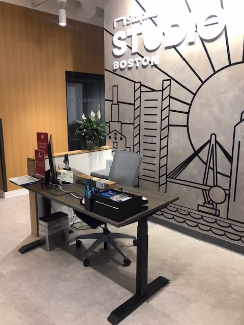 Reception desk with computer, chair, plant, and mural wall in a modern interior.