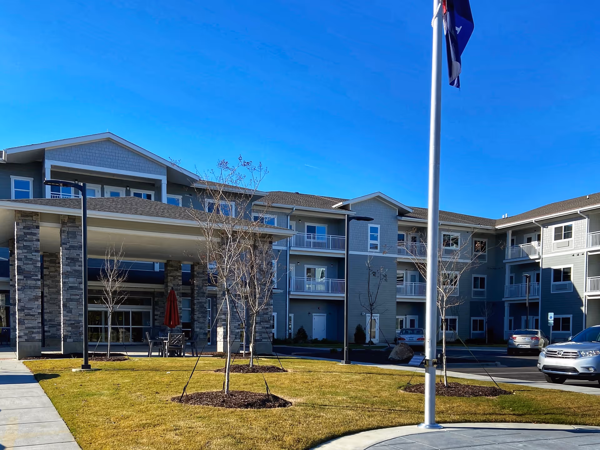 Front exterior of a multi-story retirement community building with an entrance canopy, flagpole, and landscaped lawn.