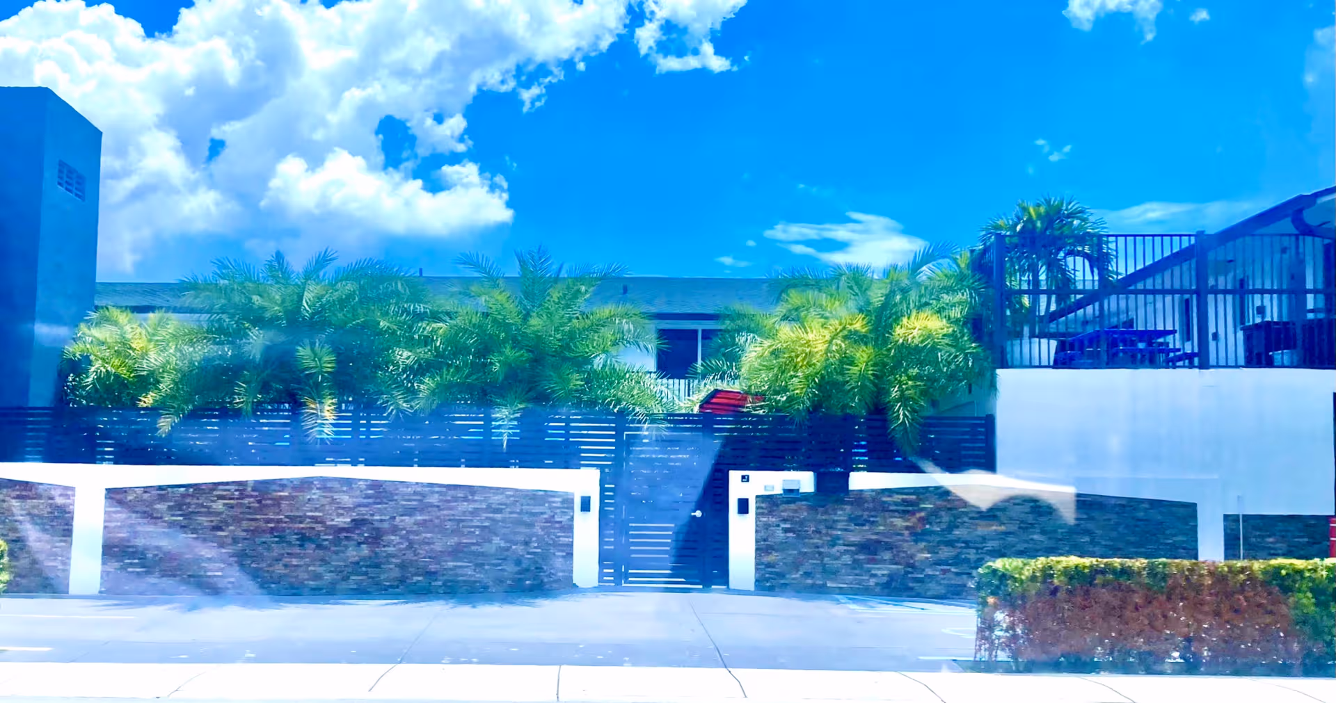 Front exterior view of Flamingo Park Manor with palm trees, stone walls, and a gated entrance