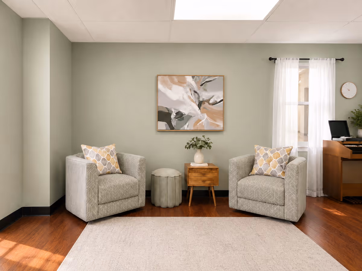 Two patterned armchairs flank a small wooden table with a plant in a green-walled living room.