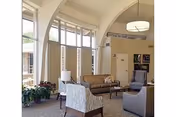 A cozy senior living lounge with arched windows, plants, and modern seating.