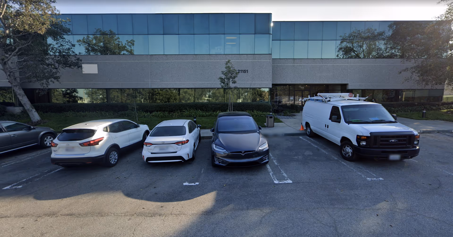 Exterior of a modern building with a parking lot and several parked vehicles.