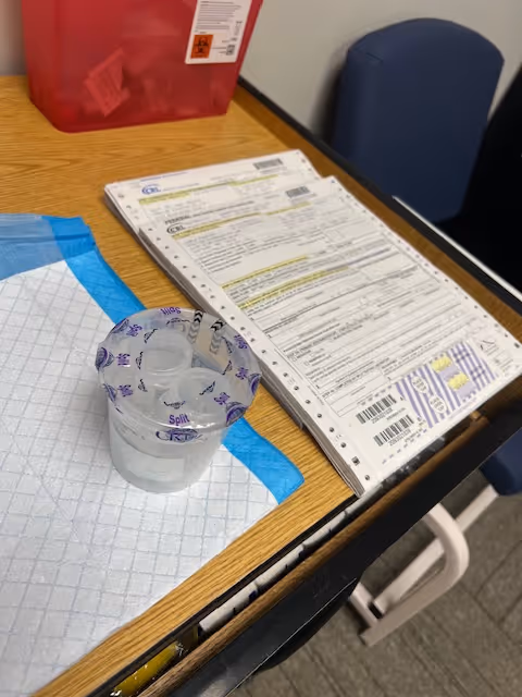 An office desk with forms, a red storage bin, a blue chair, and a plastic cup.