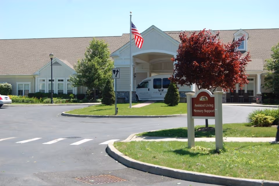 Front entrance of an assisted living residence showing a covered drop-off, American flag, landscaping and a sign for Assisted Living Memory Support.