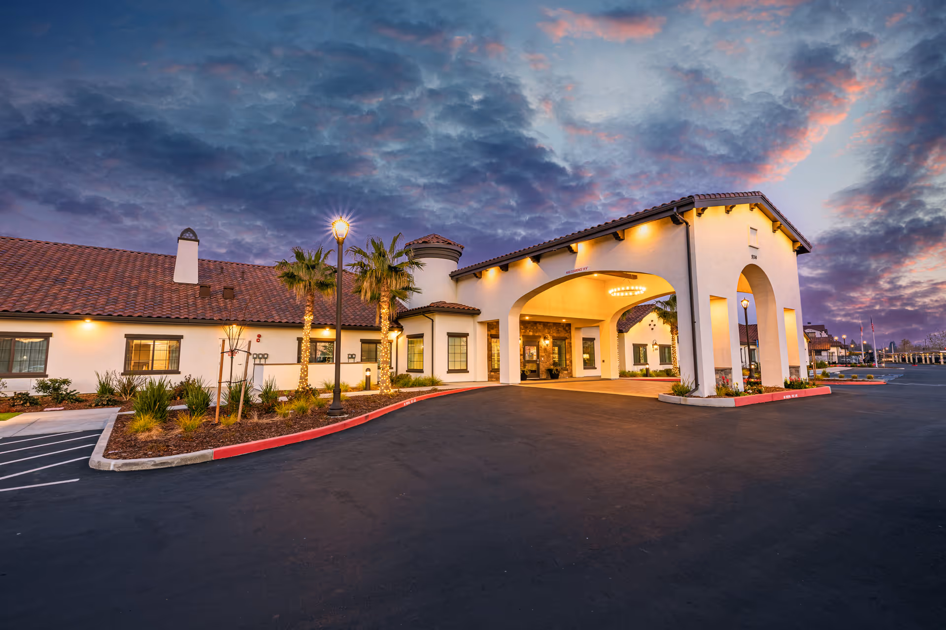 Exterior view of Gardens at Laguna Springs entrance with arches and dusk sky.