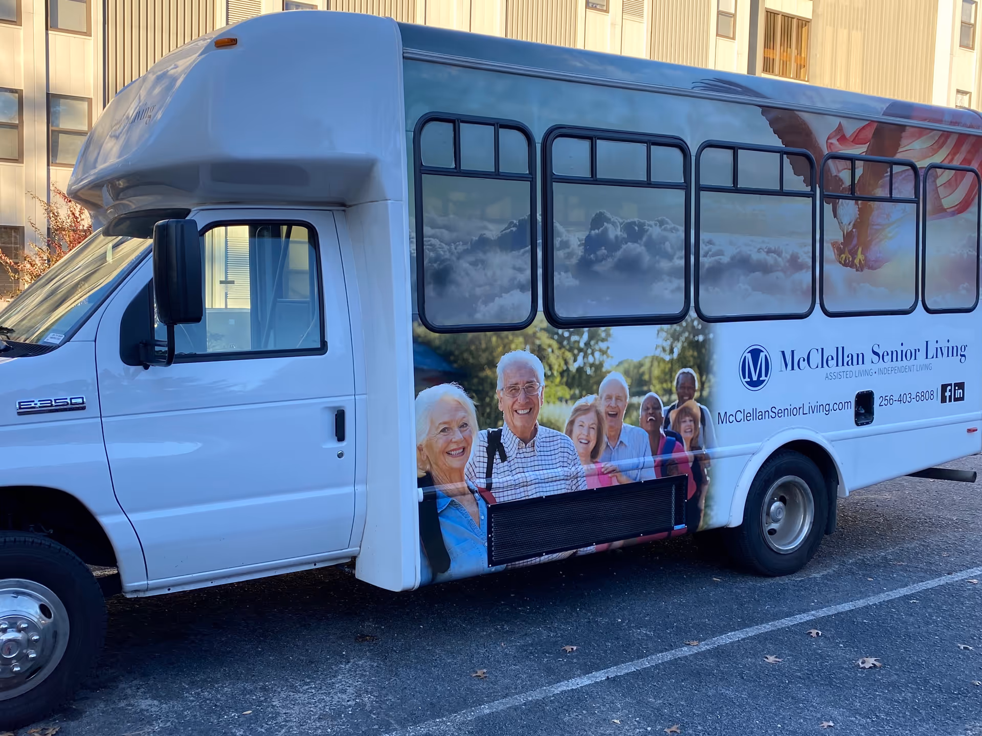White McClellan Senior Living shuttle bus with smiling senior graphics parked in a lot.