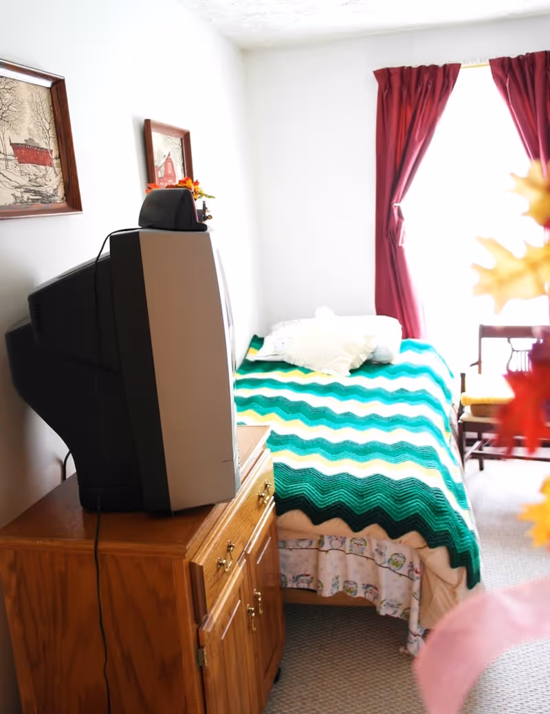 A small bedroom with a bed, dresser, vintage TV, and red curtains.